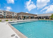 Thumbnail 18 of 34 - A large swimming pool in front of a building with a sunny sky.