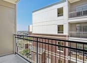 Thumbnail 32 of 33 - A balcony with a black railing overlooks a building and a clear blue sky.