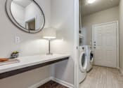 Thumbnail 15 of 30 - A laundry room with a washer and dryer, a counter, and a round mirror.