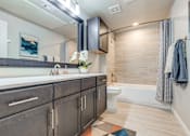 Thumbnail 13 of 30 - A bathroom with a white toilet, a sink with a mirror above it, and a bathtub with a shower curtain.