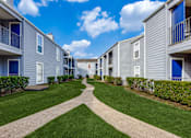 Thumbnail 24 of 27 - a walkway between two apartment buildings with green grass