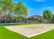 Thumbnail 26 of 30 - A sand volleyball court surrounded by a fence and trees.