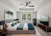Thumbnail 47 of 56 - A bedroom with a bed, a ceiling fan, a window with blinds, a painting, a potted plant, a TV, and a wooden cabinet.