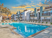 Thumbnail 1 of 38 - A swimming pool surrounded by lounge chairs and buildings in the background.