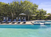 Thumbnail 7 of 14 - A pool with a waterfall and a row of sun loungers.