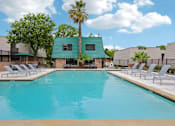 Thumbnail 14 of 21 - A large swimming pool with lounge chairs and a building with a green roof in the background.
