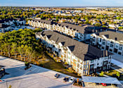 Thumbnail 9 of 25 - A large apartment complex with a parking lot in front.