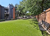 Thumbnail 24 of 28 - A grassy area with a bench and apartment buildings in the background.