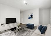Thumbnail 3 of 22 - A modern living room with a flat screen TV, a glass coffee table, and a blue ottoman.