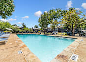Thumbnail 17 of 35 - A large swimming pool surrounded by trees and lounge chairs.