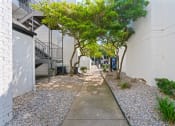 Thumbnail 25 of 28 - a walkway with trees and gravel on the side of a building