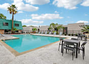 Thumbnail 16 of 21 - A pool surrounded by chairs and tables with a building in the background.