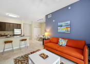Thumbnail 35 of 44 - a living room with an orange couch and a kitchen with a bar