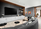 Thumbnail 24 of 25 - A modern living room with a grey sofa, a black chair, and a flat screen TV mounted on the wall.