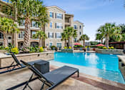 Thumbnail 31 of 42 - A black lounge chair sits in front of a pool at a resort.