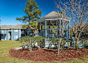 Thumbnail 29 of 35 - A gazebo is in the middle of a grassy area with a tree and shrubs around it.