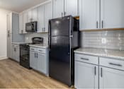 Thumbnail 9 of 11 - A black refrigerator stands in a kitchen with white cabinets and a granite countertop.