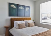 Thumbnail 27 of 27 - A bedroom with a bed, pillows, and a painting of clouds on the wall.