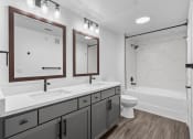 Thumbnail 11 of 25 - a bathroom with gray cabinets and a white bathtub
