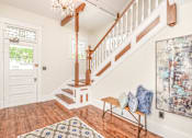 Thumbnail 11 of 23 - A staircase with a wooden banister and a chandelier hangs over a hardwood floor.