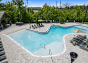 Thumbnail 22 of 35 - A large outdoor swimming pool surrounded by trees and lounge chairs.