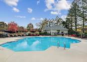 Thumbnail 24 of 45 - A large swimming pool with a blue tinted water surrounded by trees and a building in the background.