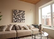 Thumbnail 4 of 15 - A living room with a couch, a table, and a painting on the wall.
