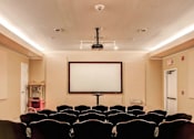 Thumbnail 18 of 22 - A row of seats in a theater with a large screen above.
