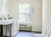 Thumbnail 19 of 22 - A room with a white desk, chairs, and a window.