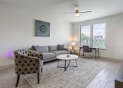 Thumbnail 2 of 20 - A living room with a grey sofa, a patterned chair, a small table, and a ceiling fan.