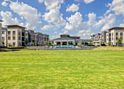 Thumbnail 13 of 33 - A large grassy field in front of apartment buildings.