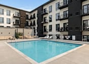 Thumbnail 10 of 35 - A large swimming pool in front of apartment buildings.