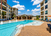 Thumbnail 7 of 35 - A swimming pool surrounded by a patio with chairs and umbrellas.