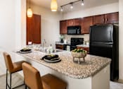 Thumbnail 24 of 35 - A kitchen with a granite countertop and a black refrigerator.