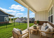 Thumbnail 11 of 38 - A patio with a sofa and chairs overlooking a green lawn and a blue house.