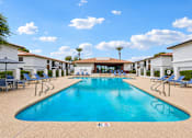 Thumbnail 21 of 26 - A large swimming pool surrounded by lounge chairs and buildings.