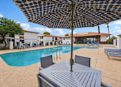 Thumbnail 22 of 26 - A pool area with a table and chairs under an umbrella.