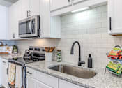 Thumbnail 24 of 41 - A kitchen with a stove, microwave, and white cabinets.