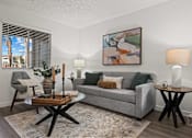 Thumbnail 4 of 23 - A living room with a grey couch, a coffee table, and a painting on the wall.