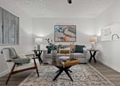 Thumbnail 5 of 23 - A living room with a grey couch, a wooden coffee table, and a painting on the wall.