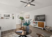 Thumbnail 6 of 23 - A living room with a ceiling fan, a couch, a coffee table, and a television.