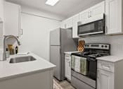 Thumbnail 2 of 23 - A modern kitchen with a stove, refrigerator, and microwave.