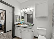 Thumbnail 21 of 29 - A bathroom with a white toilet, a sink with a mirror above it, and a shower area.
