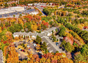Thumbnail 22 of 22 - An aerial view of a suburban area with a parking lot and houses surrounded by trees in autumn colors.