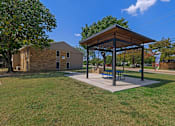 Thumbnail 13 of 16 - A pavilion with a picnic table is situated in a grassy area.