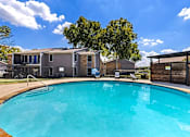 Thumbnail 11 of 16 - A swimming pool in front of a building with a blue sky and clouds in the background.
