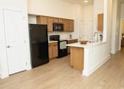 Thumbnail 2 of 28 - A black refrigerator is in the corner of a kitchen with wooden cabinets.