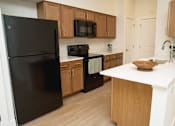 Thumbnail 7 of 28 - A black refrigerator is in a kitchen with wooden cabinets and a white counter.