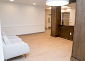 Thumbnail 27 of 28 - A hallway with a row of white chairs on the left and a wooden door on the right.