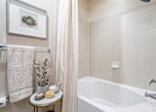 Thumbnail 30 of 35 - A bathroom with a white tub and a small table with a plant and two soaps on it.